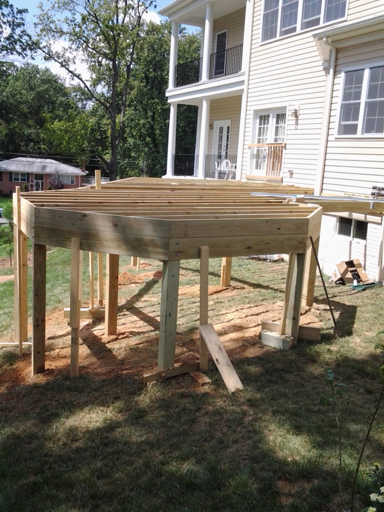 New deck framing with pressure-treated joists and posts under construction in a backyard