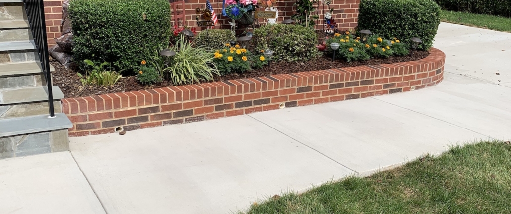 New poured concrete walkway running alongside a red brick garden wall